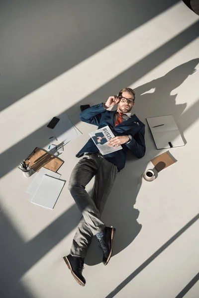 Visão de alto ângulo de jovem empresário com jornal deitado no chão — Fotografia de Stock