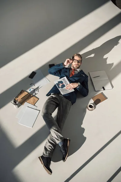 High angle view of young businessman with newspaper lying on floor — Stock Photo