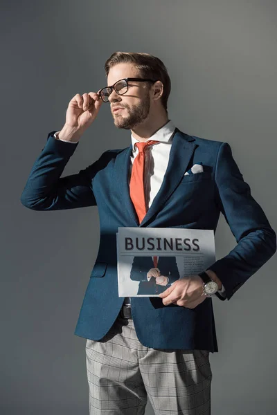 Schöner junger Mann mit Zeitung und angepasster Brille isoliert auf grau — Stockfoto