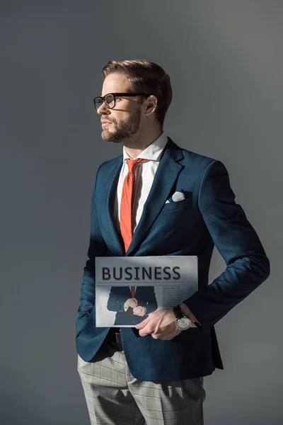 Schöner junger Geschäftsmann hält Zeitung in der Hand und schaut isoliert auf grau — Stockfoto