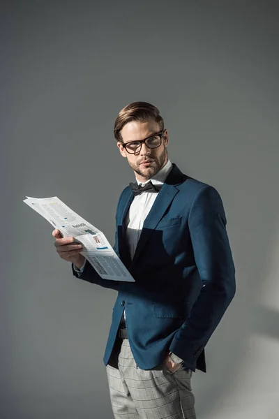 Retrato de belo homem de negócios na moda em espetáculos lendo jornal em cinza — Fotografia de Stock