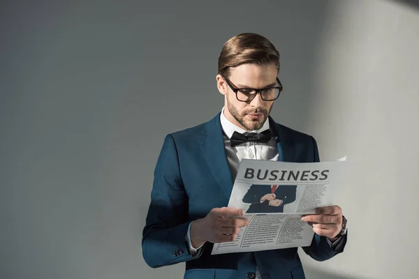 Portrait of handsome stylish businessman in spectacles reading newspaper on grey — Stock Photo