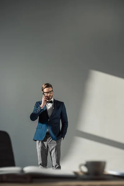 Избирательный фокус стильного бизнесмена в очках и галстуке-бабочке, разговаривающего со смартфоном — стоковое фото