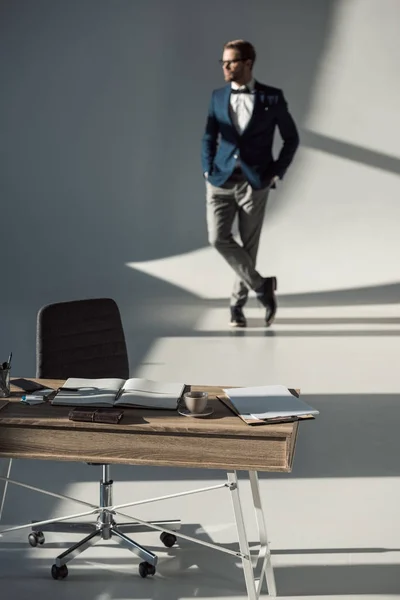 Foyer sélectif de la table avec fournitures de bureau et carnet ouvert et homme d'affaires élégant debout derrière — Photo de stock