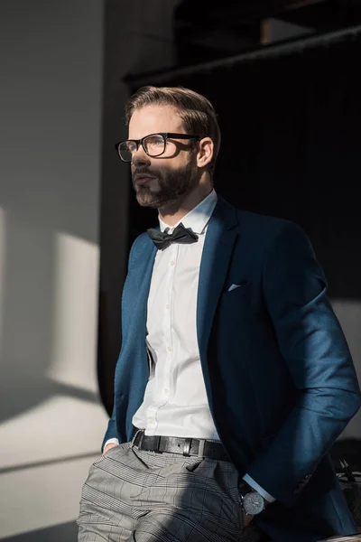 Guapo joven hombre de negocios con estilo en gafas y pajarita mirando hacia otro lado - foto de stock