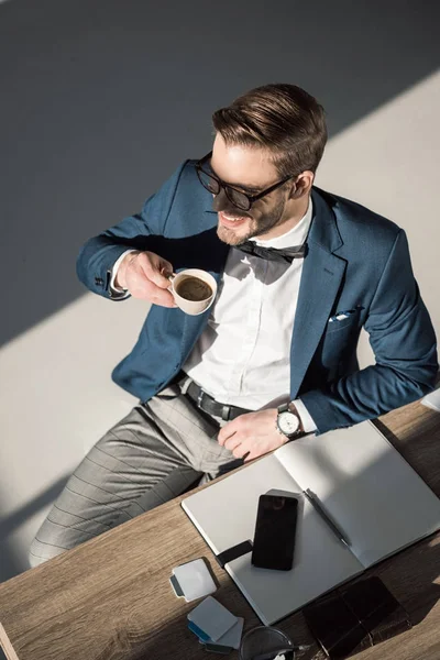 Высокий угол зрения улыбающийся молодой бизнесмен пьет кофе и смотрит в сторону — стоковое фото