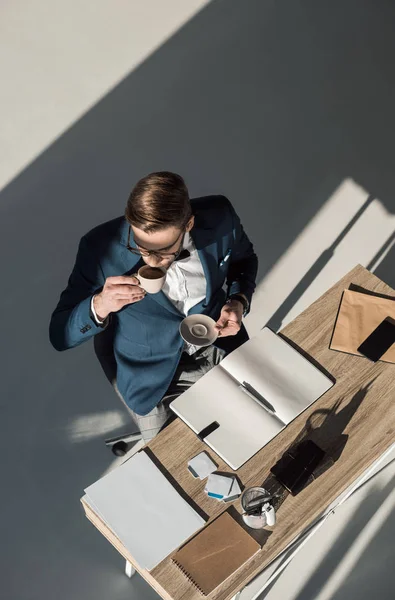 Vista aérea de joven hombre de negocios elegante beber café en el lugar de trabajo - foto de stock