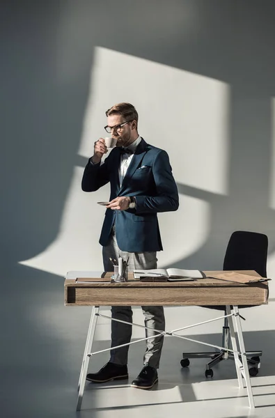 Joven hombre de negocios guapo en gafas beber café en el lugar de trabajo - foto de stock