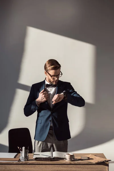 Красивий стильний молодий бізнесмен перевіряє наручний годинник на робочому місці — стокове фото