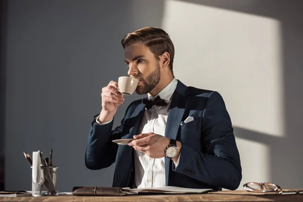 Guapo elegante joven empresario beber café en el lugar de trabajo - foto de stock