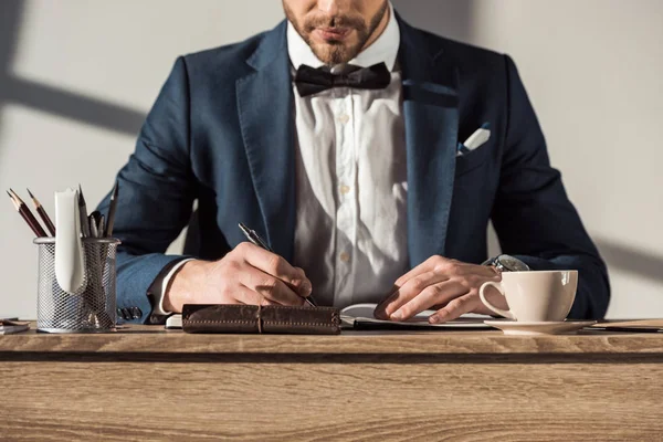 Schnappschuss eines stilvollen Geschäftsmannes in Anzug und Fliege, der in Notizbuch schreibt — Stockfoto