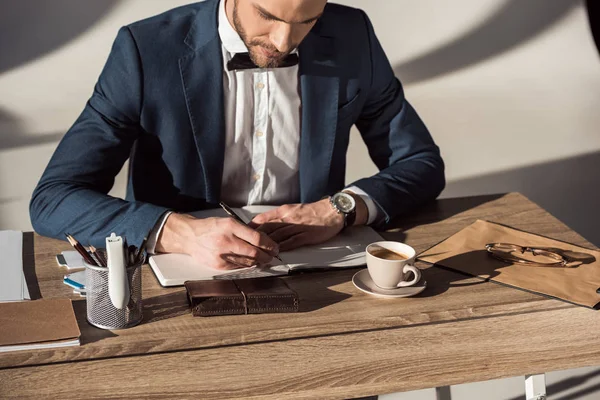 Обрізаний знімок бізнесмена, що пише в блокноті, сидячи за столом — стокове фото