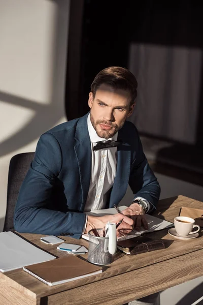 Stylish young businessman writing in diary and looking away — Stock Photo