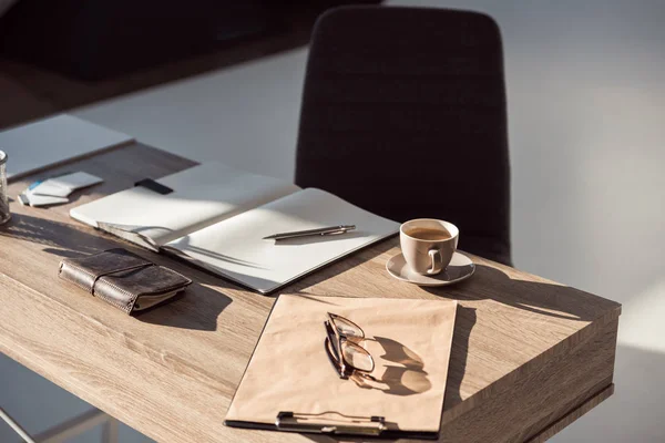 Close-up view of eyeglasses on clipboard, cup of coffee and office supplies at workplace — Stock Photo