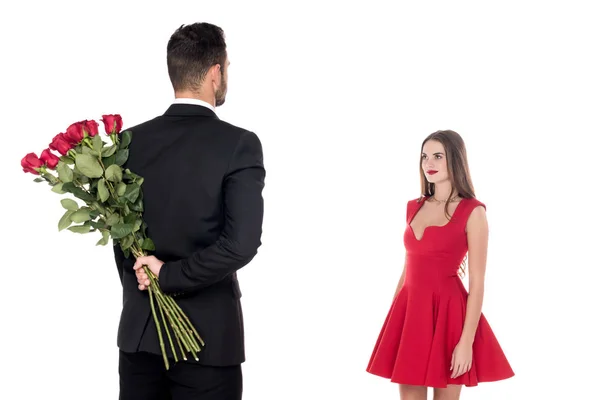 Rear view of boyfriend hiding bouquet of roses from girlfriend isolated on white — Stock Photo