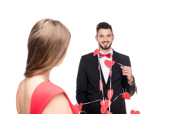 Girlfriend standing near happy boyfriend bound with garland of hearts isolated on white, valentines day concept — Stock Photo