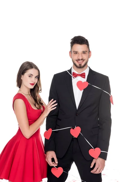 Girlfriend standing near boyfriend bound with garland of hearts isolated on white, valentines day concept — Stock Photo