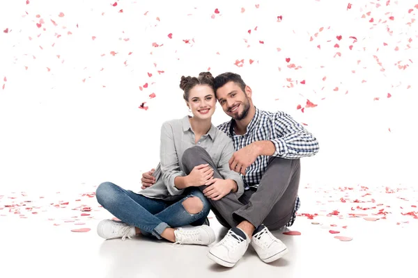 Happy couple sitting under falling confetti and hugging on white, valentines day concept — Stock Photo