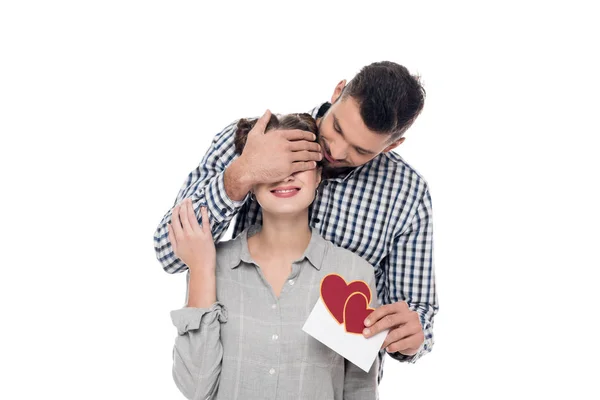 Namorado cobrindo namoradas olhos e dando cartão postal Valentim isolado no branco — Fotografia de Stock