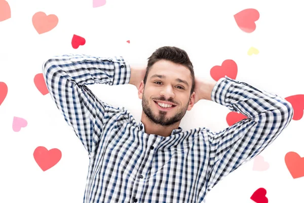 Vista aérea del hombre acostado con corazones de papel aislados en el concepto de día de San Valentín blanco - foto de stock