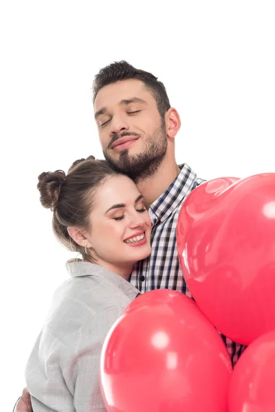 Pareja abrazando y sosteniendo globos en forma de corazón aislados en blanco, día de San Valentín concepto - foto de stock