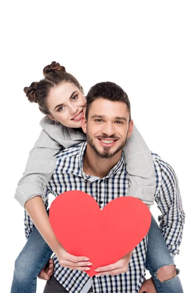 Namorado dando piggyback para namorada segurando coração vermelho isolado no branco, dia dos namorados conceito — Fotografia de Stock