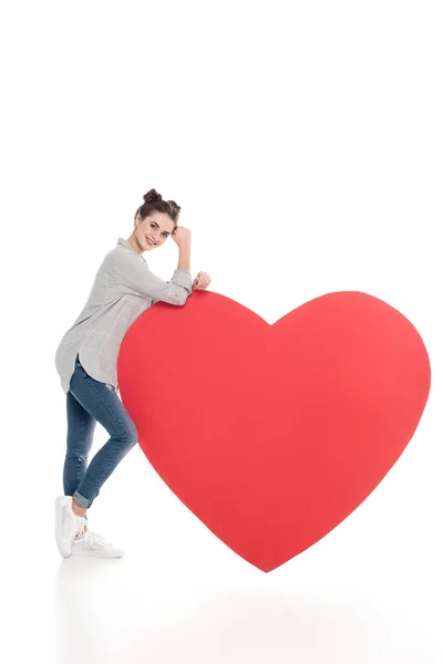 Smiling girl leaning on big heart on white, valentines day concept — Stock Photo