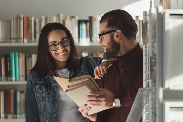 Sorridente coppia multiculturale con libri in biblioteca — Foto stock