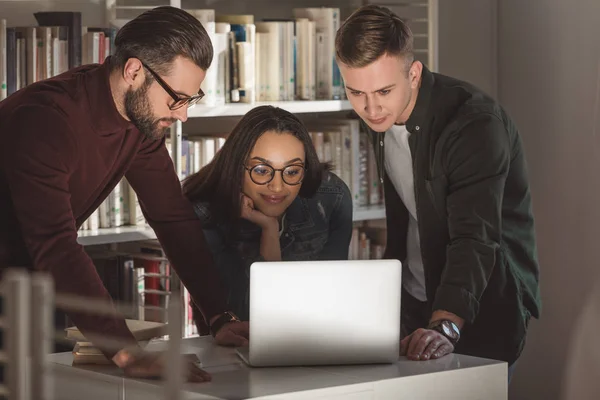 Multikulti-Freunde schauen in Bibliothek auf Laptop — Stockfoto