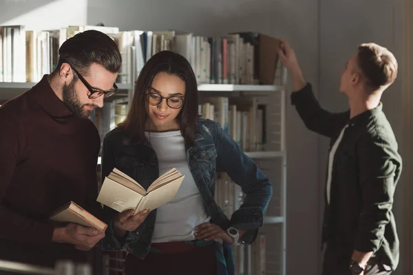 Multikulti-Freunde schauen sich Buch in Bibliothek an — Stockfoto