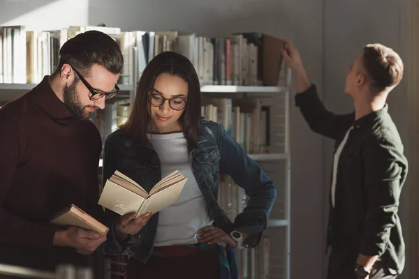 Amigos multiculturales mirando el libro en la biblioteca - foto de stock