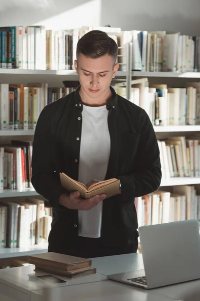 Schöne Studentin steht und liest Buch in Bibliothek — Stockfoto