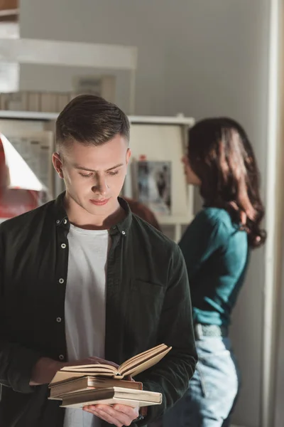 Beau étudiant debout et le livre de lecture dans la bibliothèque — Photo de stock