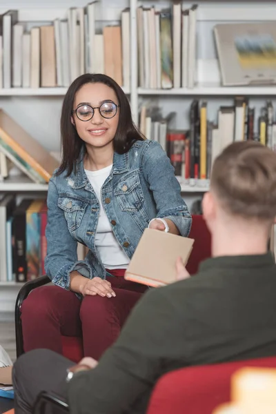 Souriant amis multiculturels partageant un livre dans la bibliothèque — Photo de stock