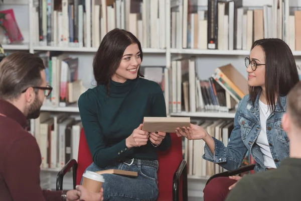 Amigos multiculturales sonrientes compartiendo libro en la biblioteca - foto de stock