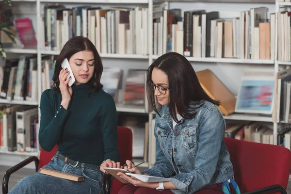 Привлекательная девушка разговаривает по смартфону в библиотеке — стоковое фото