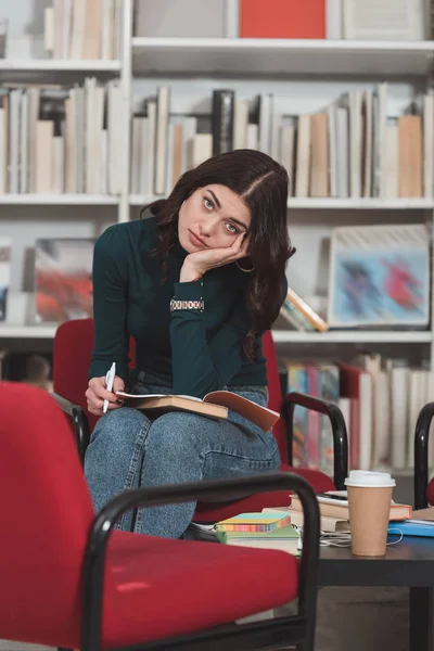 Müder Student sitzt auf Stuhl in Bibliothek und blickt in Kamera — Stockfoto
