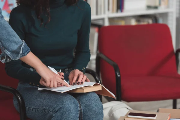 Recortado imagen de chica señalando algo en cuaderno de amigos en la biblioteca - foto de stock