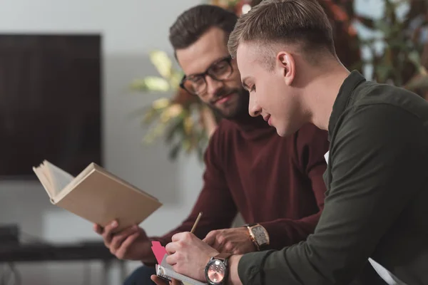 Amis masculins étudiant avec ordinateur portable et livre — Photo de stock