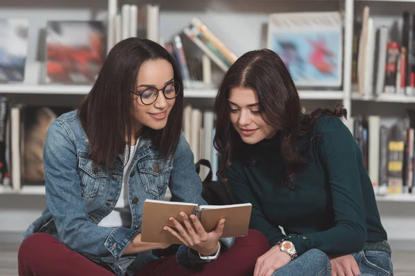 Meninas multiculturais olhando para notebook na biblioteca — Fotografia de Stock