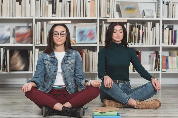 Мультикультурные девушки медитируют с книгами о головах в библиотеке — стоковое фото