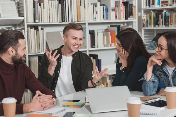 Lächelnde multikulturelle Freunde unterhalten sich in der Bibliothek — Stockfoto