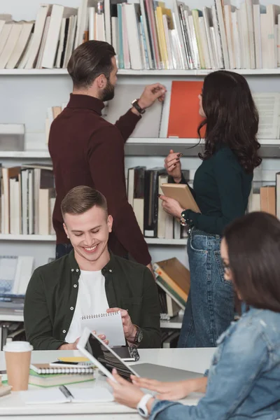 Étudiants souriants étudiant dans la bibliothèque avec tablette et ordinateur portable — Photo de stock