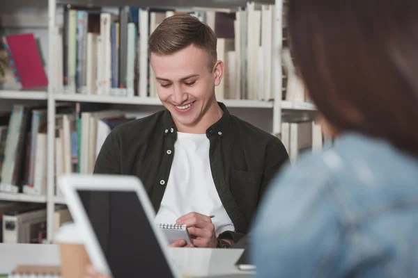 Smiling student writing something to notebook in library — Stock Photo