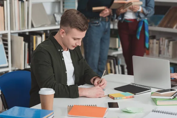 Studente scrivere qualcosa per notebook in biblioteca — Foto stock