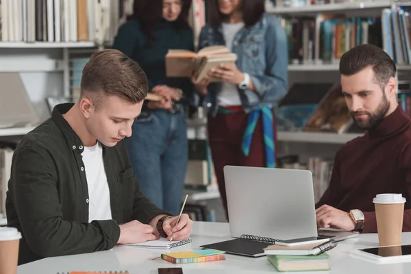 Estudiantes varones que estudian en la biblioteca con portátil - foto de stock