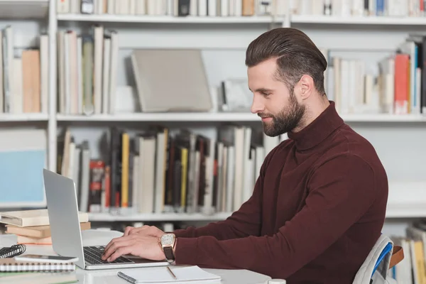 Side view of handsome student using laptop in library — Stock Photo