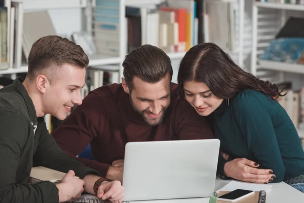 Smiling friends looking at laptop in library — Stock Photo