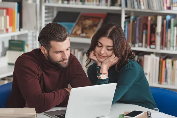 Boyfriend and girlfriend studying together in library and using laptop — Stock Photo