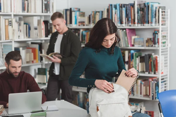 Studentin packt Notizbuch in Tasche in Bibliothek — Stockfoto